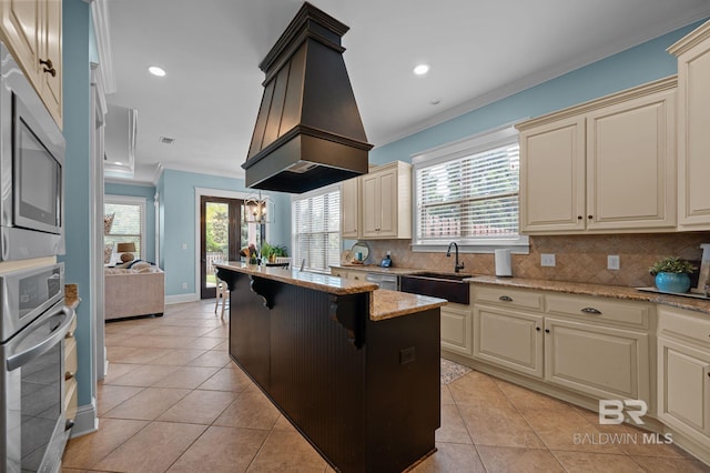 kitchen with cream cabinetry, ornamental molding, stainless steel appliances, and a sink