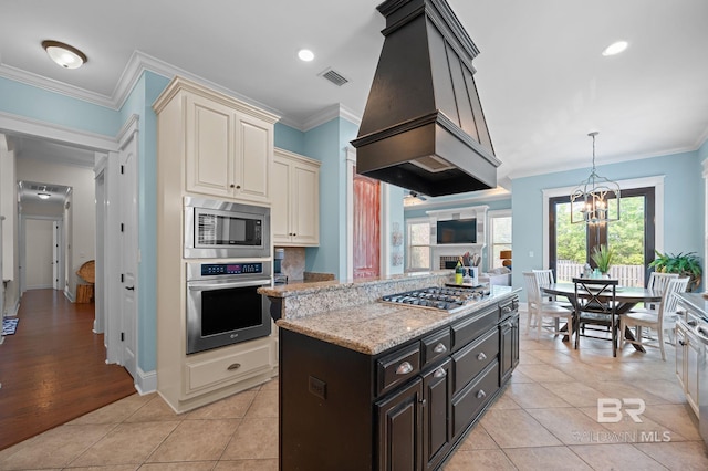 kitchen featuring appliances with stainless steel finishes, custom range hood, light stone countertops, light tile patterned floors, and cream cabinets