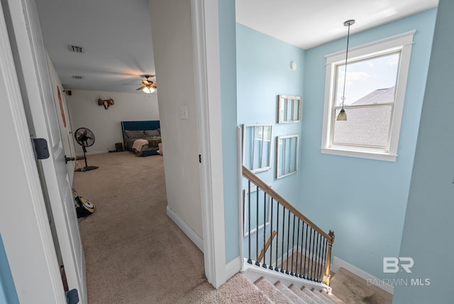 corridor with carpet floors, visible vents, baseboards, and an upstairs landing