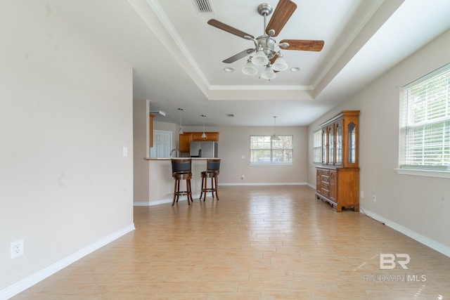 living area with ornamental molding, baseboards, ceiling fan, light wood-type flooring, and a tray ceiling
