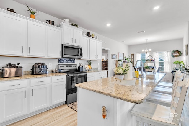 3905 Mercury Cir, Gulf Shores, AL 36542 - kitchen featuring an island with sink, stainless steel appliances, a notable chandelier, white cabinets, and light stone counters