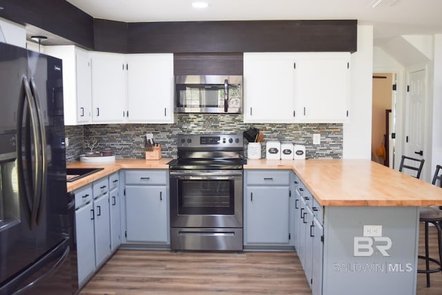 kitchen featuring hardwood / wood-style flooring, tasteful backsplash, white cabinets, a breakfast bar, and appliances with stainless steel finishes