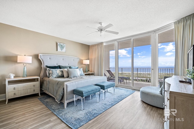 bedroom with a wall of windows, access to outside, a textured ceiling, and wood finished floors