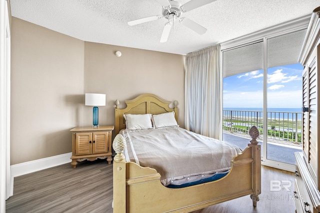 bedroom with a water view, a textured ceiling, wood finished floors, access to outside, and baseboards