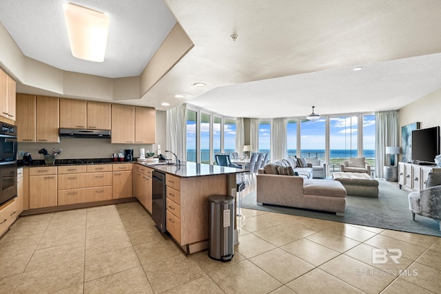 kitchen with light brown cabinetry, expansive windows, a peninsula, dishwasher, and under cabinet range hood