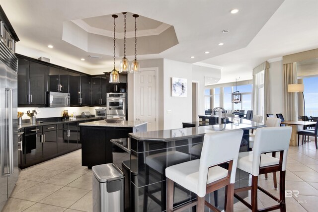 14237 Perdido Key Dr Unit Ph-1401, Pensacola, FL 32507 - kitchen with light tile patterned flooring, a breakfast bar area, a tray ceiling, a center island with sink, and dark cabinets