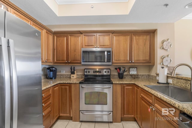 kitchen with stainless steel appliances, sink, light tile patterned floors, light stone counters, and a textured ceiling