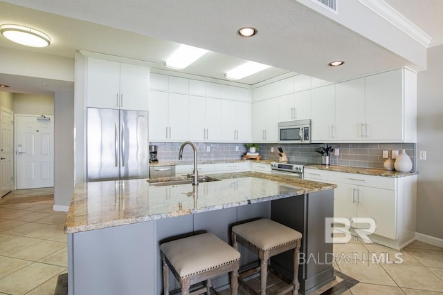 kitchen featuring a kitchen breakfast bar, light tile patterned floors, stainless steel appliances, backsplash, and a sink