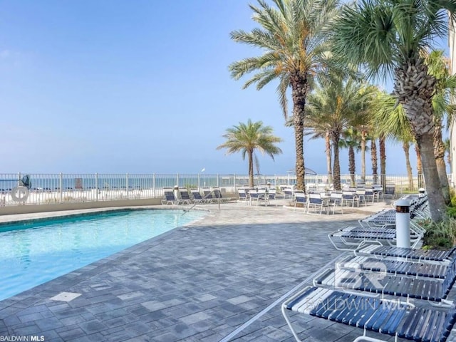 community pool featuring a water view, fence, and a patio