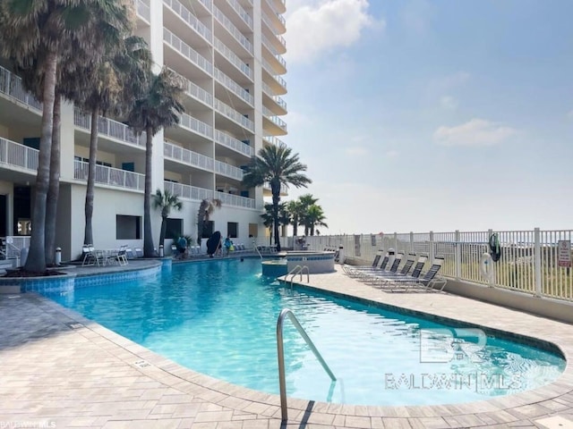 community pool with a patio, a hot tub, and fence