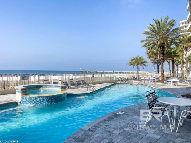 view of pool featuring fence, a pool with connected hot tub, a water view, and a patio area