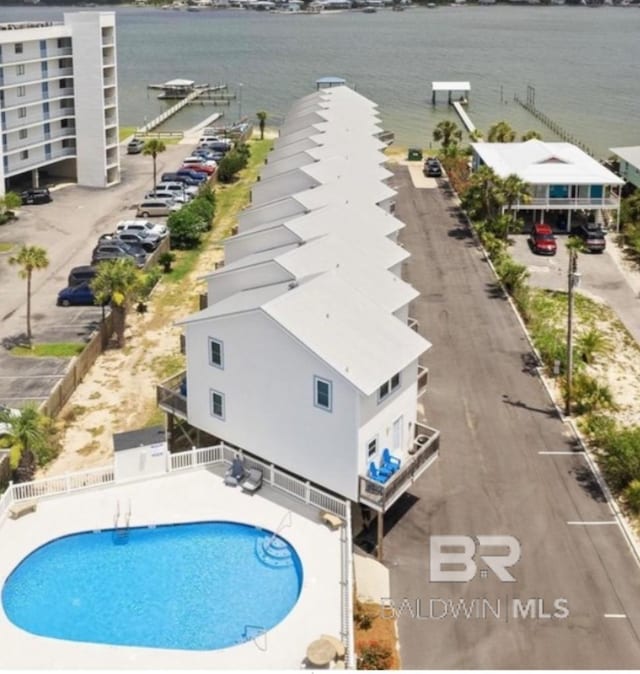 community pool featuring a patio area, a water view, and fence