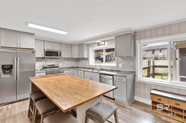 kitchen featuring sink, light hardwood / wood-style flooring, stainless steel appliances, tasteful backsplash, and a kitchen bar