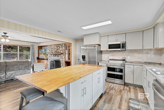 kitchen featuring white cabinetry, stainless steel appliances, a kitchen breakfast bar, a fireplace, and ornamental molding