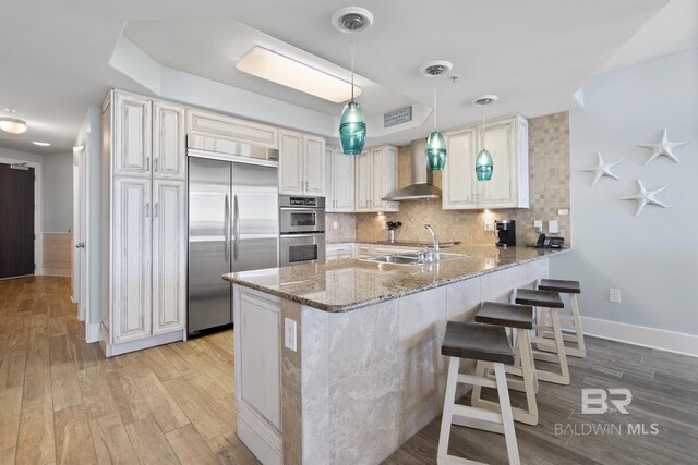 28107 Perdido Beach Blvd Unit D512, Orange Beach, AL 36561 - kitchen with appliances with stainless steel finishes, wall chimney range hood, a peninsula, light stone counters, and light wood-style floors