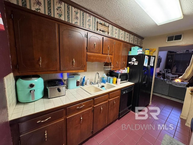 kitchen with tile countertops, visible vents, a sink, a textured ceiling, and black appliances