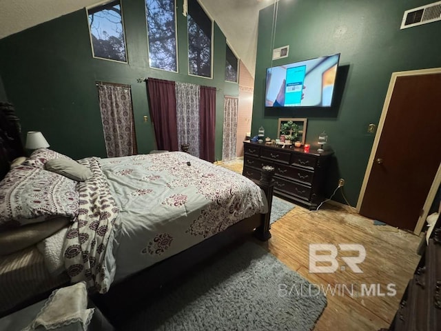 bedroom with high vaulted ceiling, visible vents, and wood finished floors