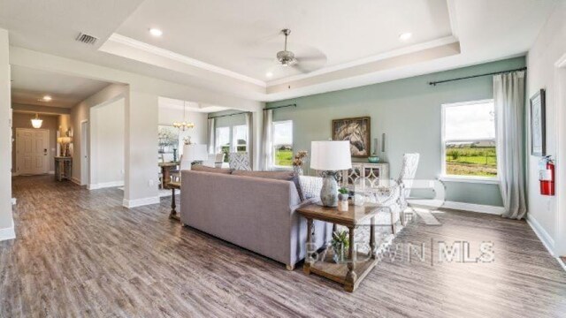 living room featuring hardwood / wood-style flooring, a tray ceiling, ceiling fan with notable chandelier, and crown molding