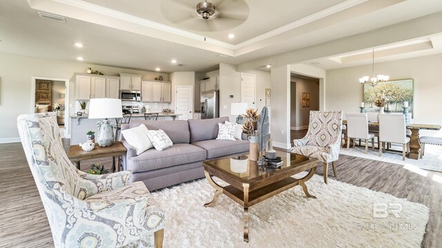 living room with ornamental molding, a raised ceiling, ceiling fan with notable chandelier, and light wood-type flooring