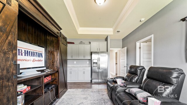 living room with crown molding, a tray ceiling, a barn door, and light wood-type flooring