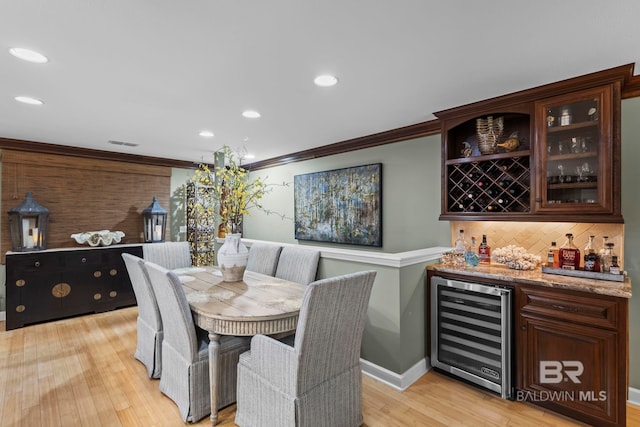 dining room with visible vents, ornamental molding, wine cooler, bar, and light wood finished floors