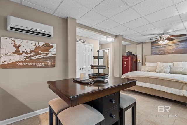 bedroom featuring light tile patterned floors, baseboards, an AC wall unit, and a paneled ceiling