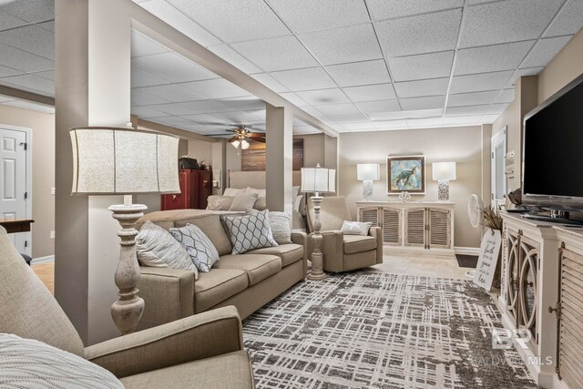 living area with baseboards, ceiling fan, and a paneled ceiling