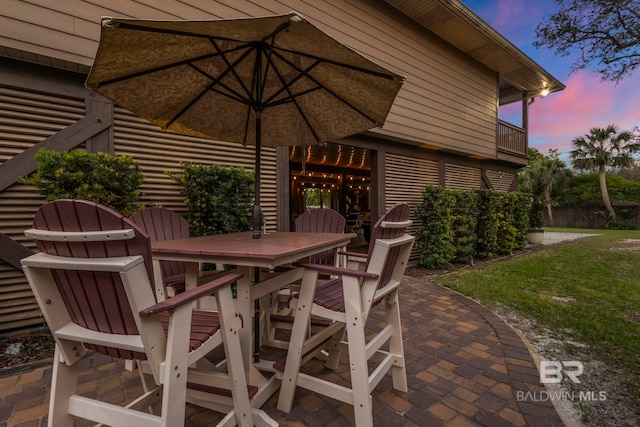 patio terrace at dusk featuring fence, outdoor dining area, and a yard