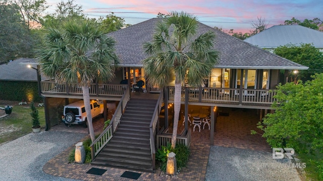 back of property at dusk with covered porch, stairs, a shingled roof, driveway, and a carport