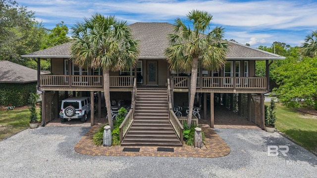 raised beach house featuring a porch, a shingled roof, driveway, and a carport