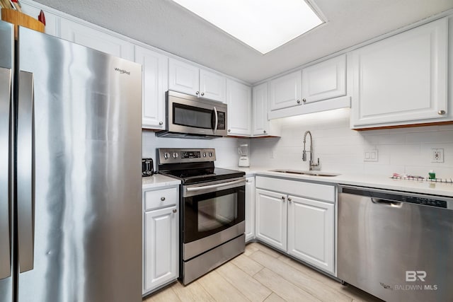 kitchen with sink, white cabinets, backsplash, stainless steel appliances, and light hardwood / wood-style flooring