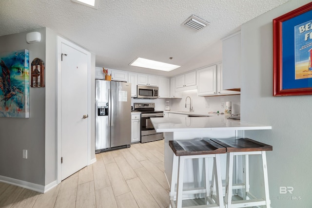 kitchen with appliances with stainless steel finishes, white cabinetry, sink, kitchen peninsula, and a textured ceiling