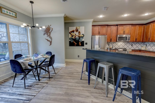 kitchen with a chandelier, light hardwood / wood-style flooring, tasteful backsplash, ornamental molding, and appliances with stainless steel finishes