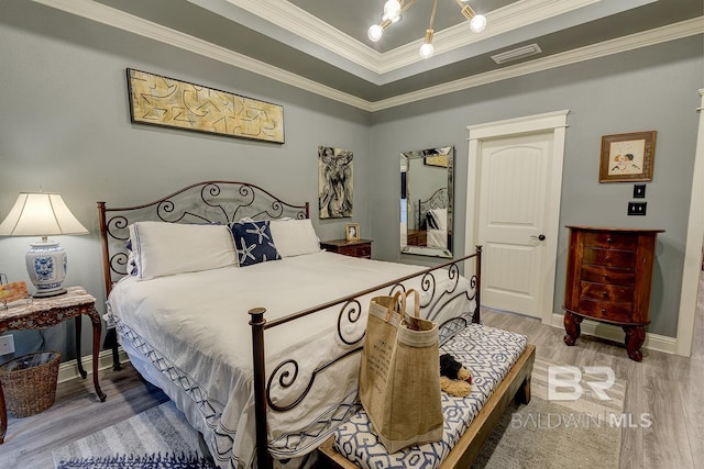 bedroom with a tray ceiling, hardwood / wood-style flooring, ornamental molding, and an inviting chandelier