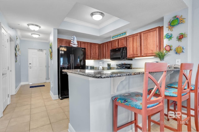 kitchen with light tile patterned floors, a raised ceiling, ornamental molding, a breakfast bar, and black appliances