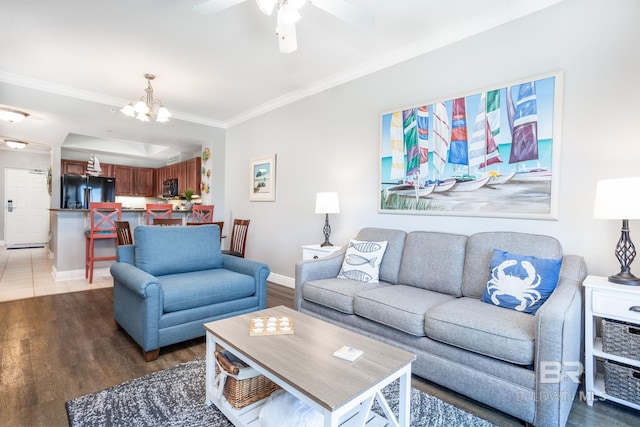 living room featuring baseboards, ornamental molding, wood finished floors, a tray ceiling, and ceiling fan with notable chandelier