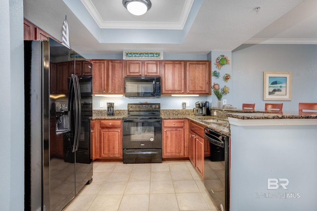 kitchen with ornamental molding, a tray ceiling, dark stone counters, and black appliances