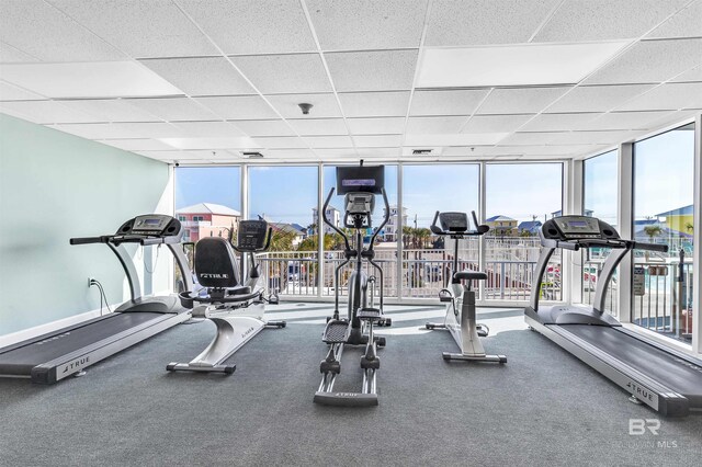 gym with baseboards, floor to ceiling windows, a drop ceiling, and a wealth of natural light