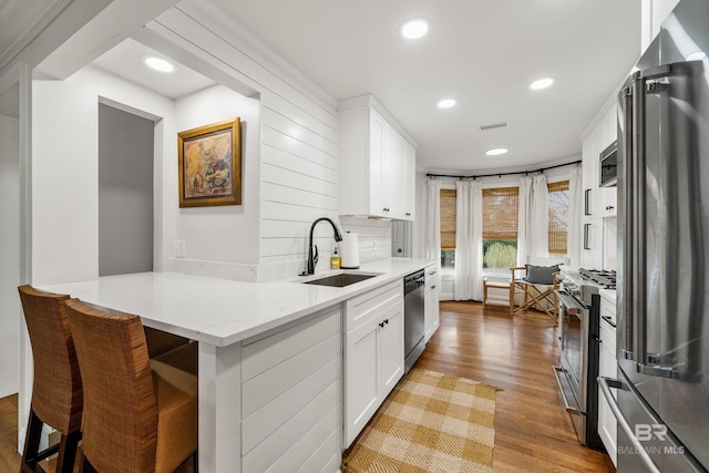 kitchen featuring high quality appliances, a sink, wood finished floors, white cabinets, and recessed lighting