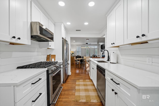 kitchen featuring stainless steel appliances, a sink, light wood-style floors, white cabinets, and recessed lighting