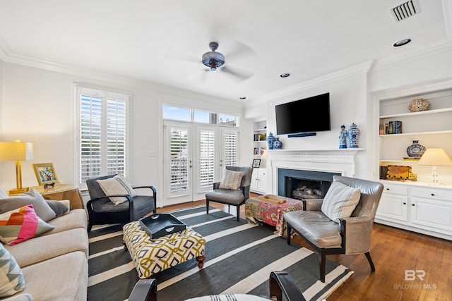living room featuring crown molding, a ceiling fan, dark wood-style floors, a fireplace, and built in features
