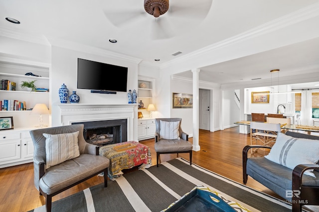 living area with ornamental molding, wood finished floors, ceiling fan, built in shelves, and a fireplace