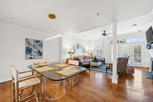 dining room with crown molding, wood finished floors, a fireplace, a ceiling fan, and baseboards