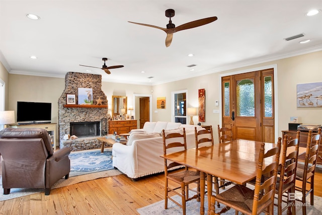 dining space with a stone fireplace, crown molding, light hardwood / wood-style flooring, and ceiling fan