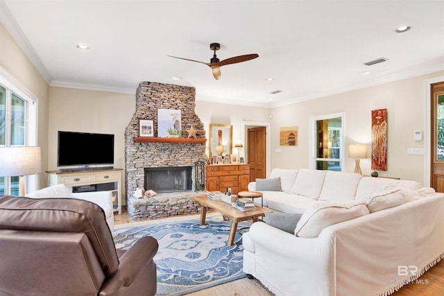 living room with crown molding, a fireplace, ceiling fan, and light wood-type flooring