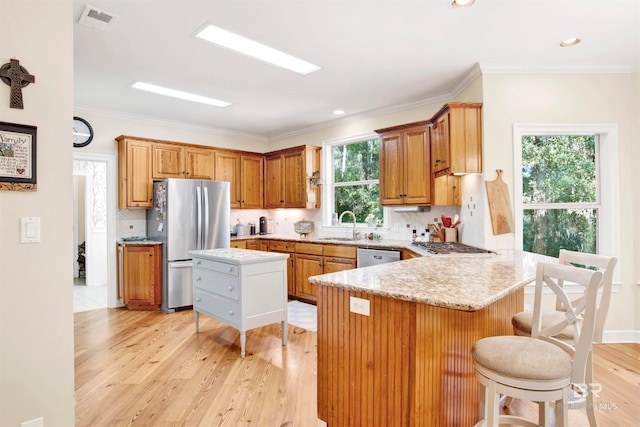 kitchen with kitchen peninsula, plenty of natural light, stainless steel appliances, and light hardwood / wood-style floors