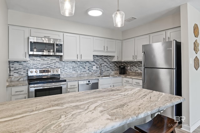 kitchen with a kitchen bar, appliances with stainless steel finishes, decorative backsplash, white cabinets, and hanging light fixtures