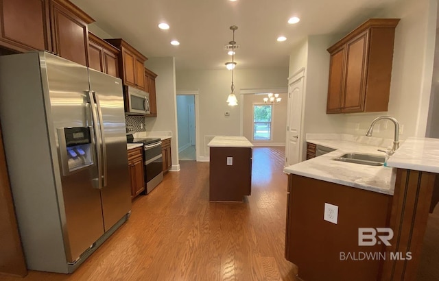 kitchen featuring sink, decorative light fixtures, light hardwood / wood-style flooring, appliances with stainless steel finishes, and a kitchen island