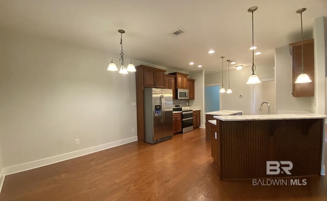 kitchen featuring dark hardwood / wood-style flooring, decorative backsplash, hanging light fixtures, kitchen peninsula, and stainless steel appliances