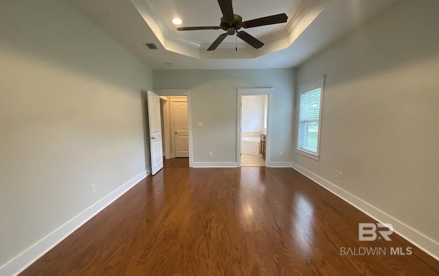 unfurnished bedroom with ceiling fan, ensuite bathroom, ornamental molding, dark hardwood / wood-style flooring, and a raised ceiling